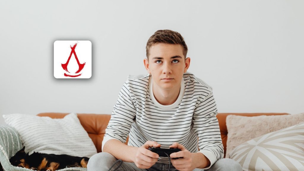 A man sitting on a couch holding a game controller, ready to dive into an Assassin’s Creed Shadows session or write a game review while parents relax nearby.